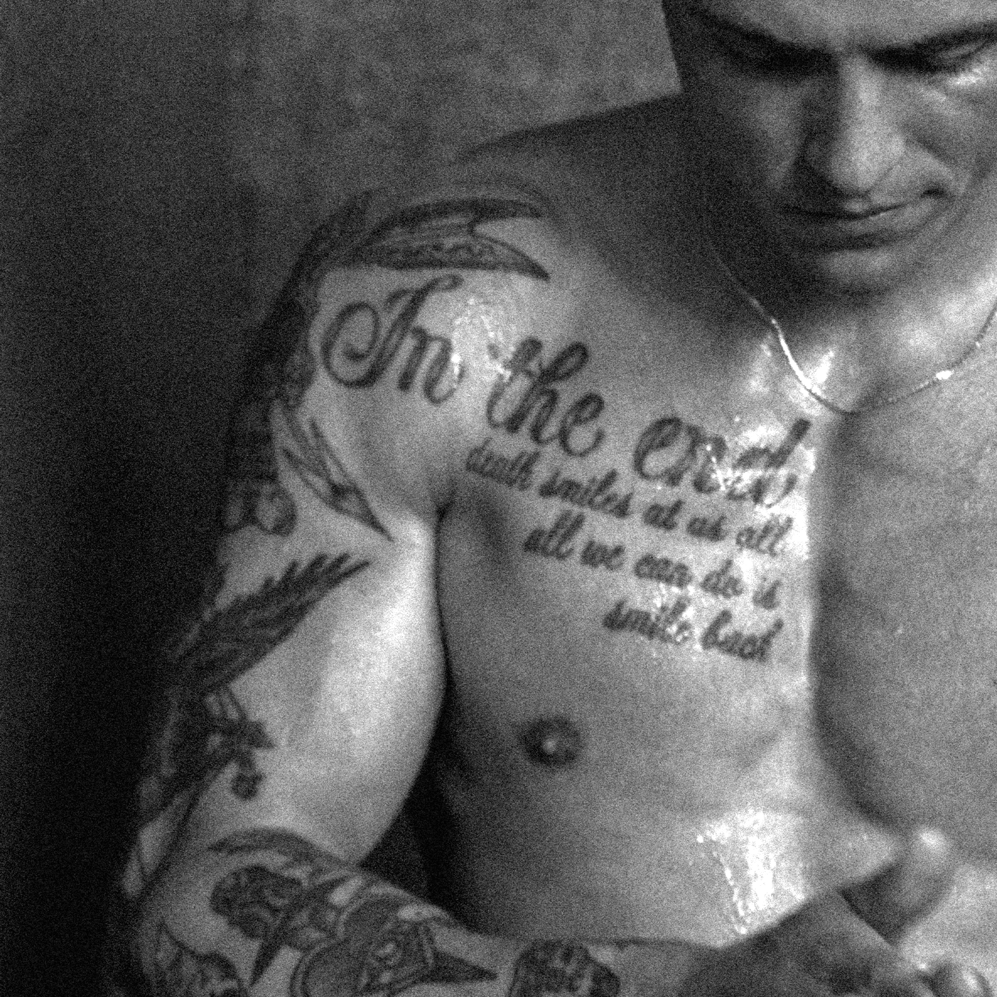A close-up of a man with tattoos, focusing on his upper body and the chest tattoo that reads 'In the end, death smiles at us all.'