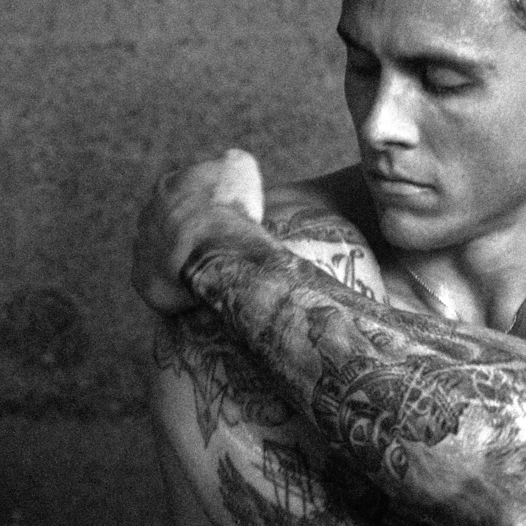 A man applying CLEANSING BODY WASH [TRAVEL] on tattooed arm in a shower.